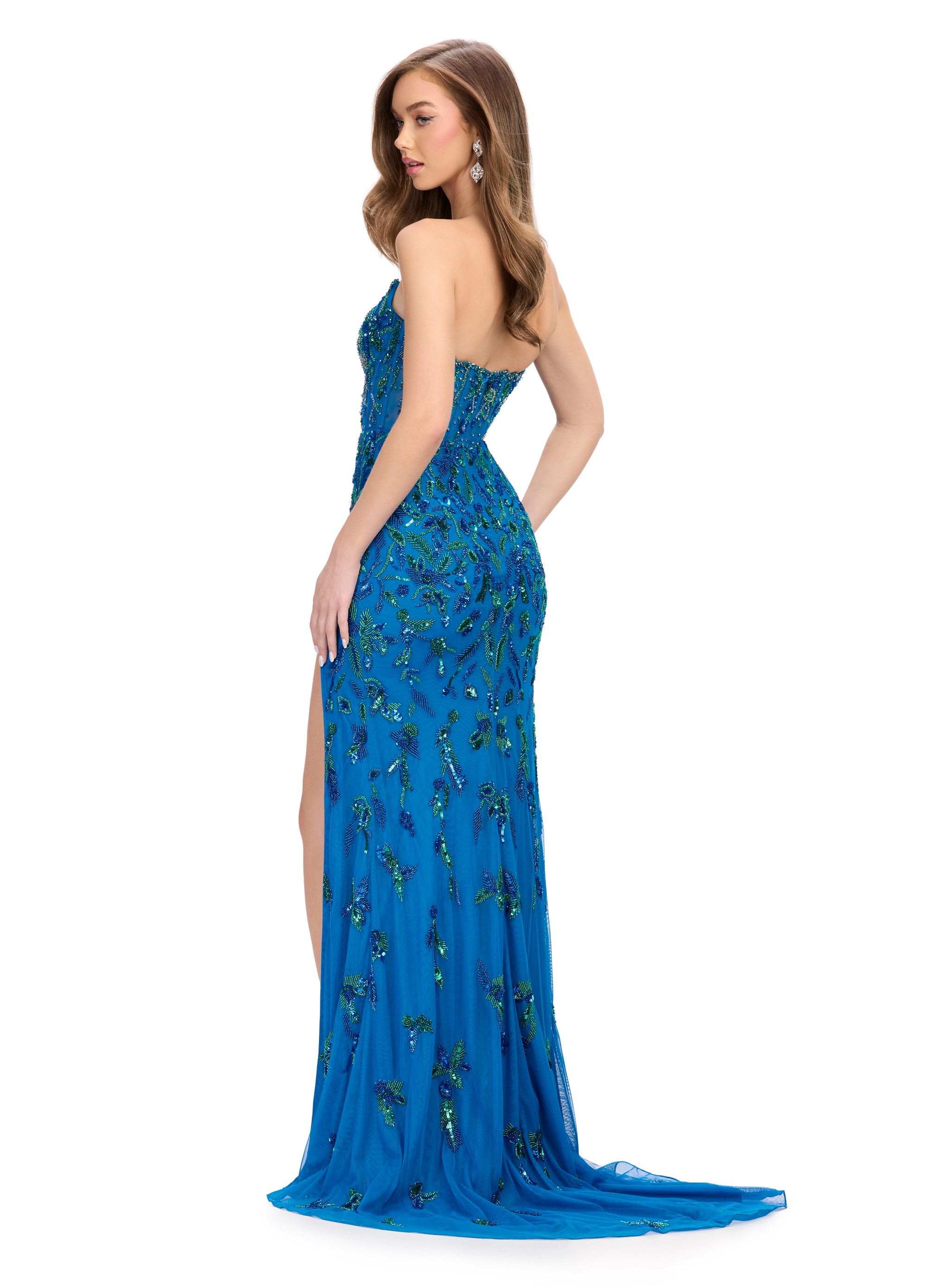Back view of a stunning royal blue strapless gown adorned with intricate green beaded embellishments, featuring a structured bodice, a high slit, and a sheer overlay for an elegant and captivating look.