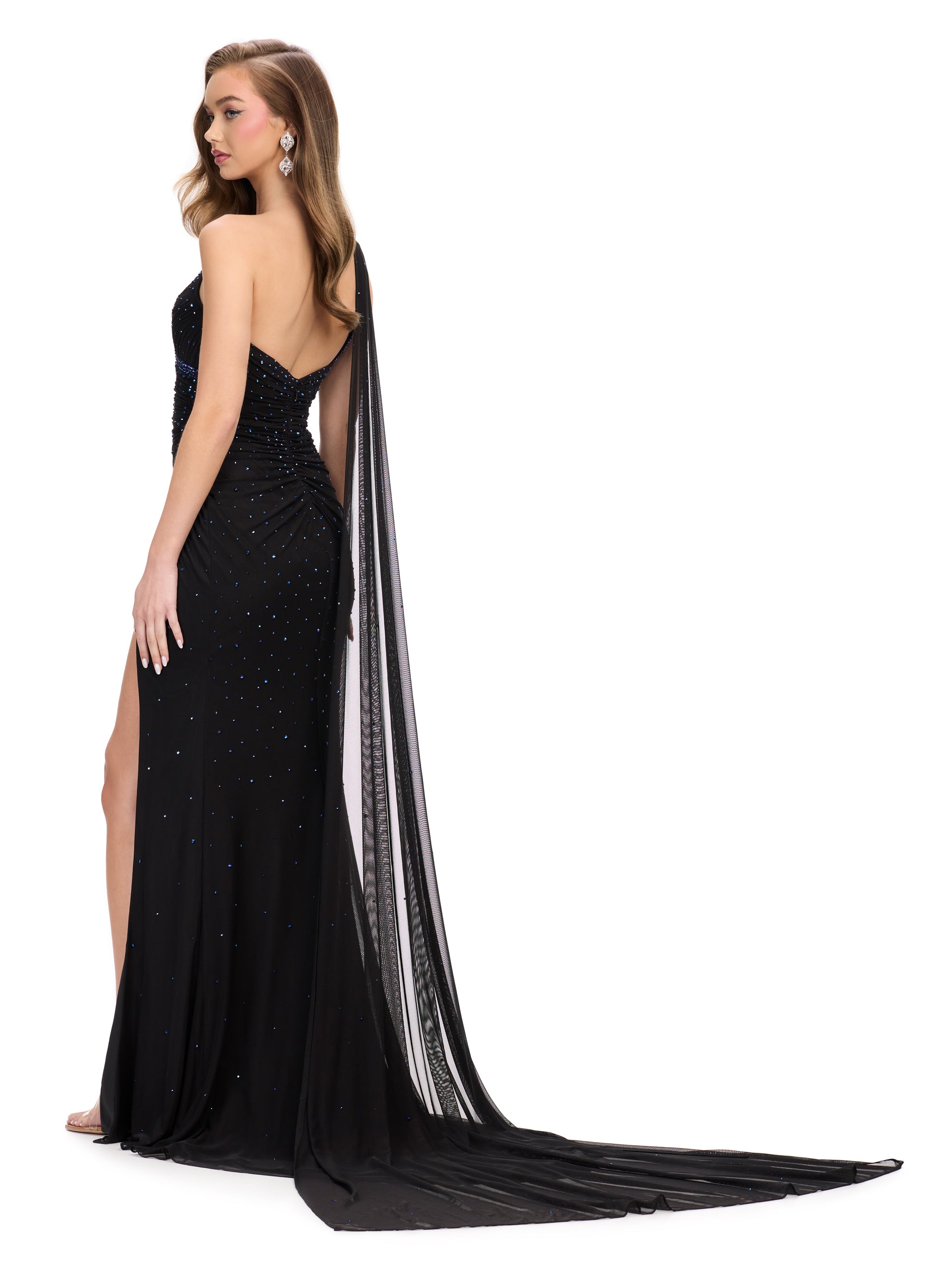 Back view - Black asymmetric one-shoulder evening gown adorned with scattered embellishments, featuring a draped bodice, thigh-high slit, and a flowing sheer cape for a dramatic and elegant silhouette.