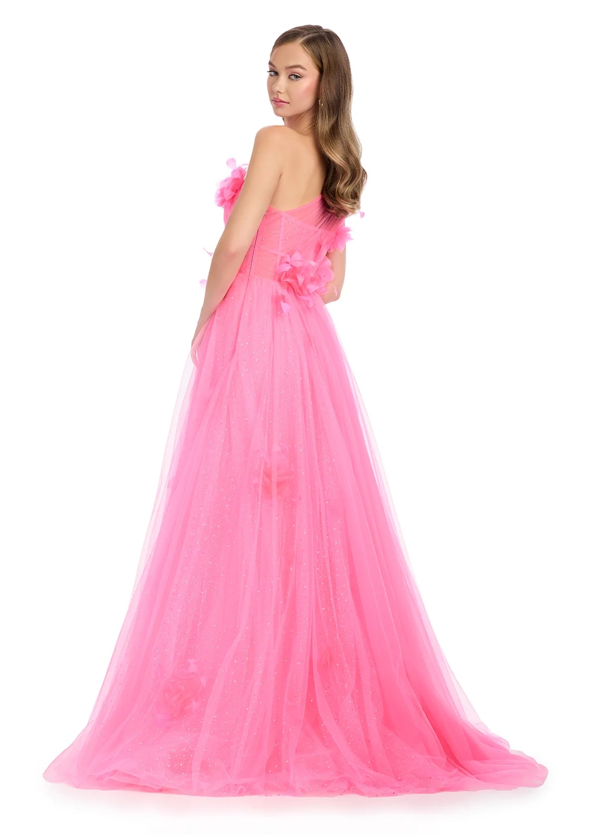 Back view of a hot pink one-shoulder ball gown featuring delicate tulle layers adorned with soft floral appliqués, a semi-sheer corset bodice, and a romantic flowy skirt that glimmers subtly, perfect for an enchanting evening.