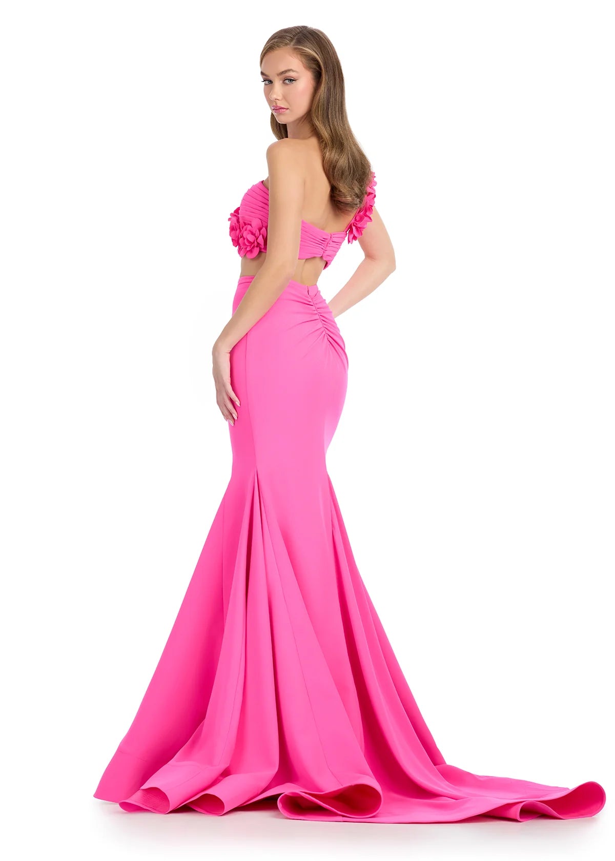 Back view of a hot pink two-piece gown featuring a strapless floral-embellished crop top and a fitted mermaid skirt with a dramatic flared hemline.