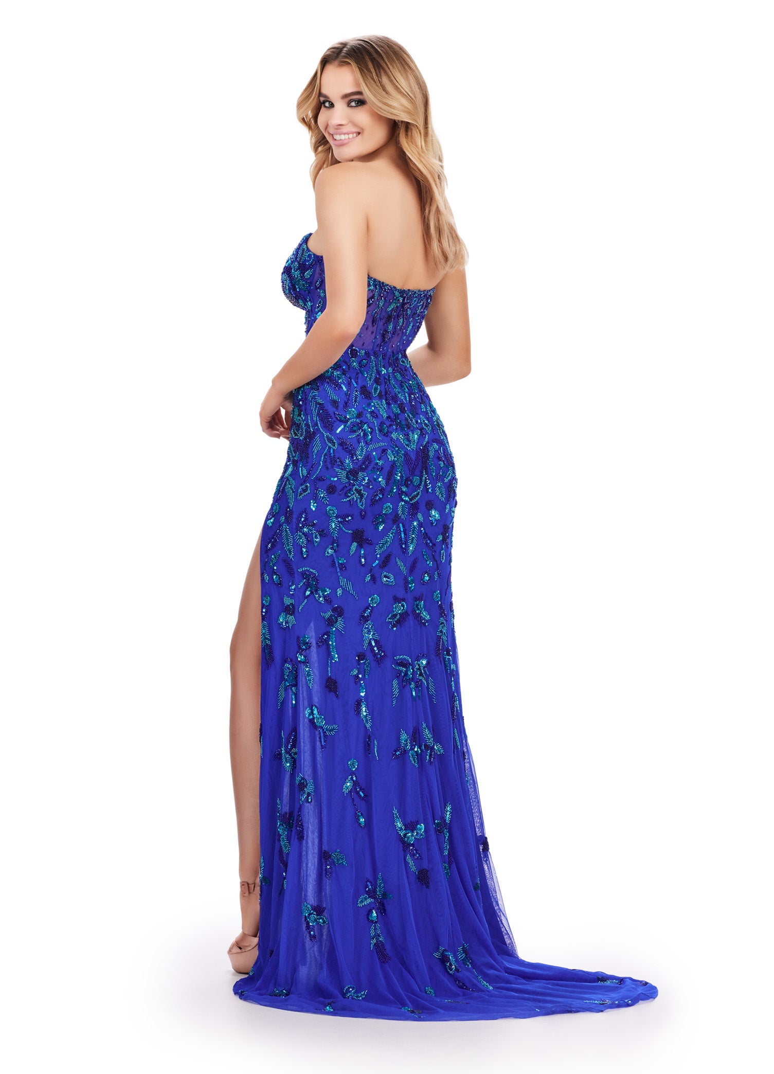 Back view of a stunning royal blue strapless gown adorned with intricate green beaded embellishments, featuring a fitted bodice, a thigh-high slit, and a sheer overlay for a captivating and glamorous look.